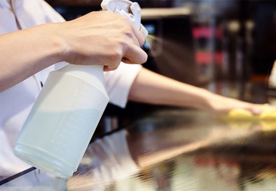 A person sprays a non-labeled disinfectant spray on a countertop.